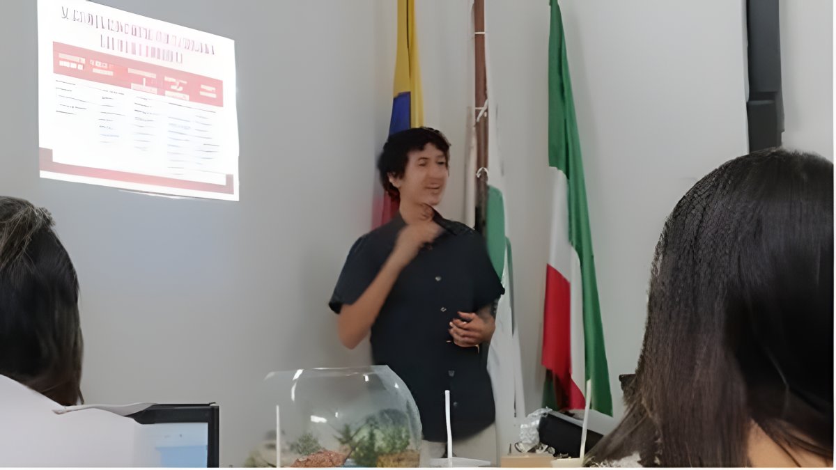 Un ponente expone ante un auditorio junto a una proyección y las banderas de Colombia y el Caquetá.
