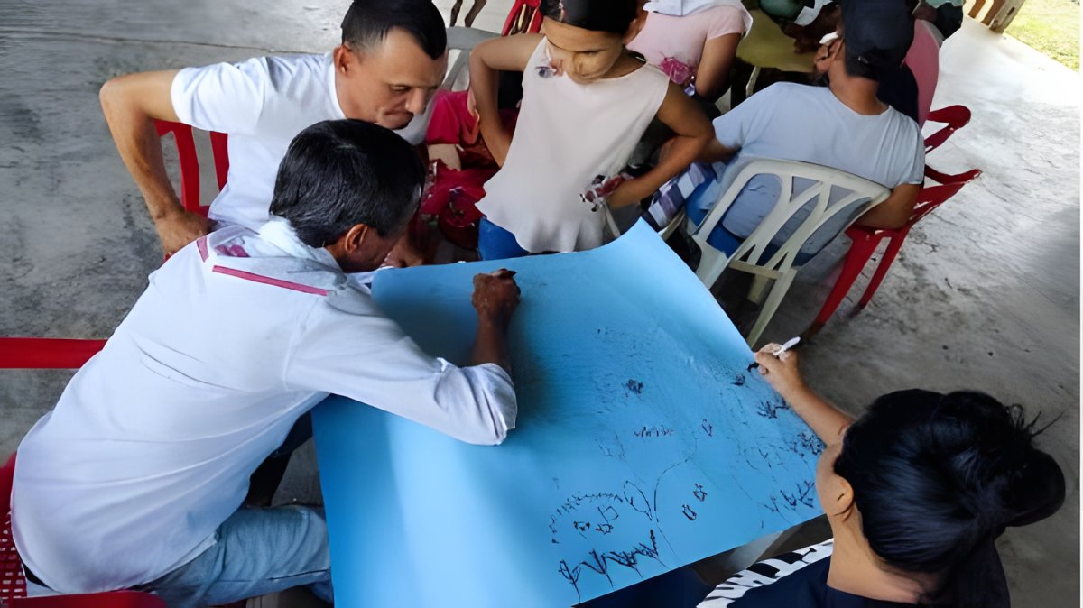 Varias personas dibujan juntas sobre una cartulina azul en un taller alrededor de una mesa.