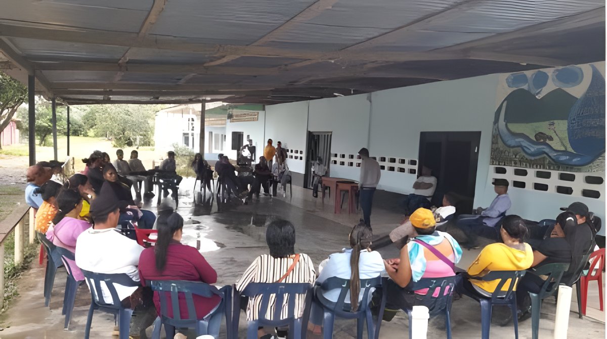 Una reunión comunitaria en círculo bajo un cobertizo, junto a una pared con un mural pintado.