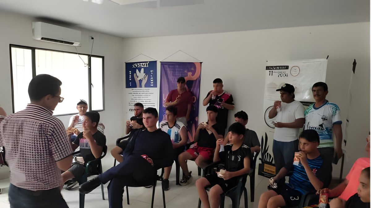 Un facilitador se dirige a un grupo de jóvenes sentados en un salón, junto a varios pendones.