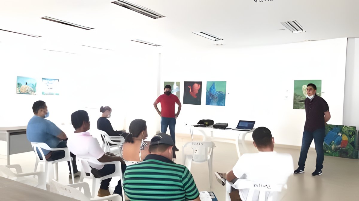 Un grupo escucha a dos expositores en una sala con cuadros de fauna y paisaje colgados en la pared.