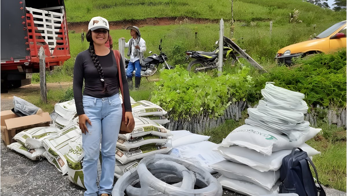 Una mujer posa junto a bandejas de plántulas y sacos de insumos al borde de una vía.